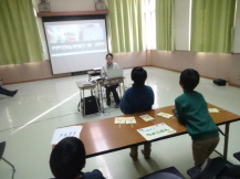 長机の上にパソコンを置いて、その机の前に集まった子供たちがオンラインクイズを楽しんでいる様子の写真