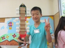 水色のTシャツの男の子がピースをしながら右手に自分の作品を持っている写真