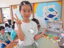 自分で作った作品を左手に持ちながらピース姿で笑顔の女の子の写真