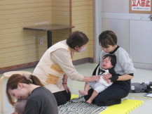 お母さんの膝の上に座っている赤ちゃんにベビーマッサージをしている先生の写真