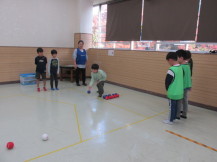 緑色のビブスを着ている子たちが見ている中、相手チームの男の子が青いボールを投げようとしている写真