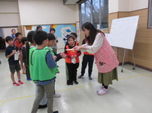 ピンク色のエプロンを身に付けている女性から、ビブスを付けたチームの子が賞状を受け取っている写真