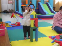 自分と同じ背の高さまで積み木を積んで遊んでいる幼い女の子の写真
