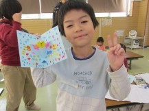 右手でピースサインをしながら、左手に持った雨模様のカードをカメラに見せている男の子の写真
