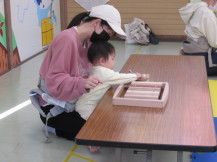 お母さんの膝の上に座っていろいろな木でできた木琴をたたいている赤ちゃんの写真