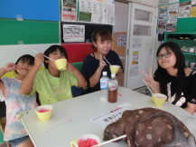 机の周りに4人の女の子が並んで座りかき氷を食べながらピースをしたりして楽しんでいる写真