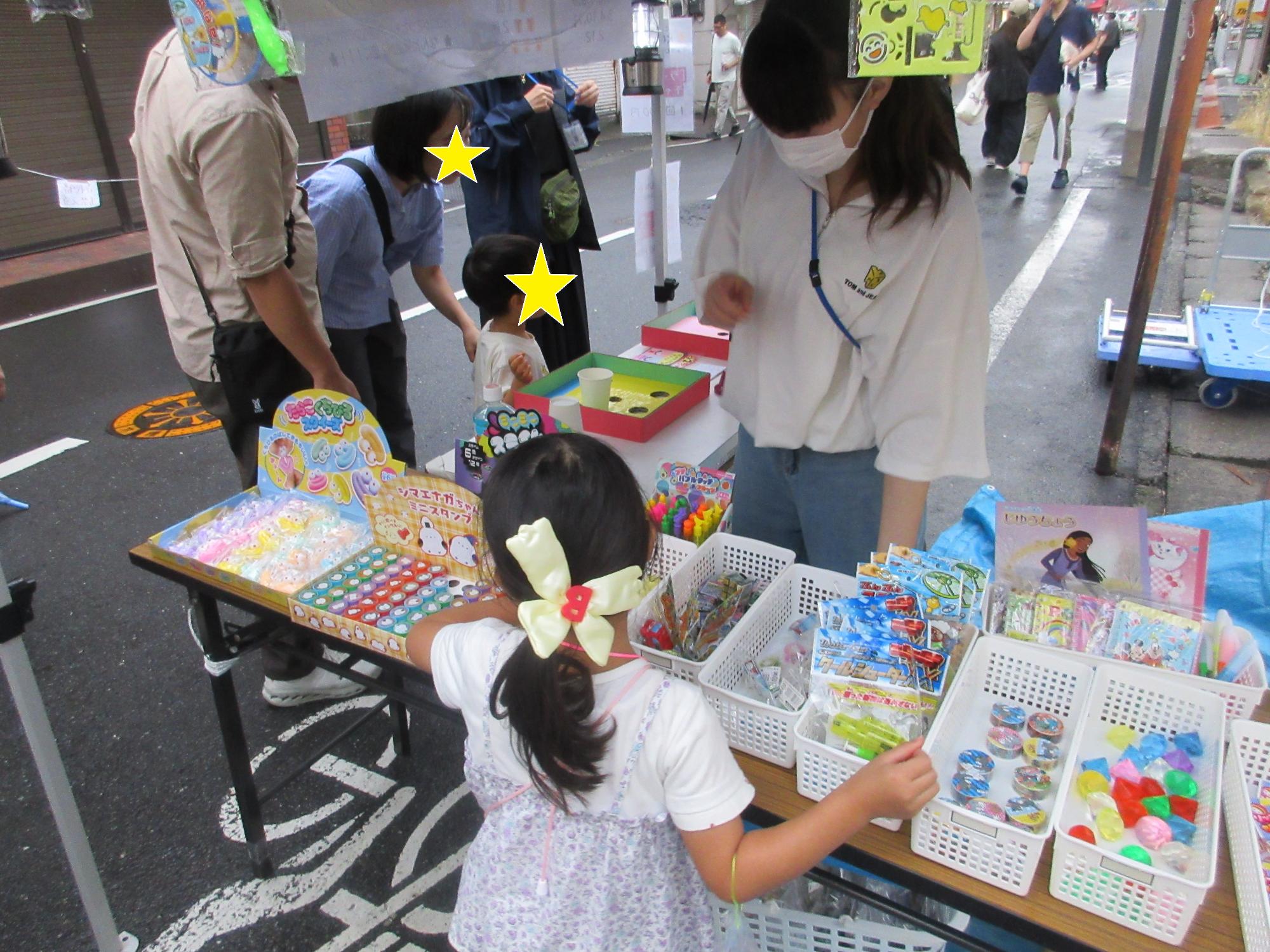 テーブルに並んだスクイーズやスライム、すたんぷ、きらきらボールやシールなどたくさんの中から景品を選ぶ子ども