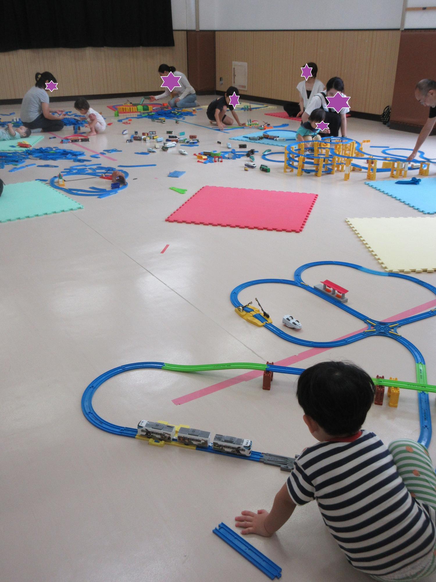 集会室で自分たちで作ったプラレールに電車を走らせてあそぶ親子たち