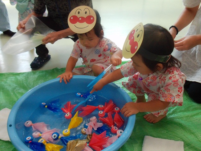 家庭用の子どもプールを設置し、釣りに見立てて遊んでいる数組の親子の写真