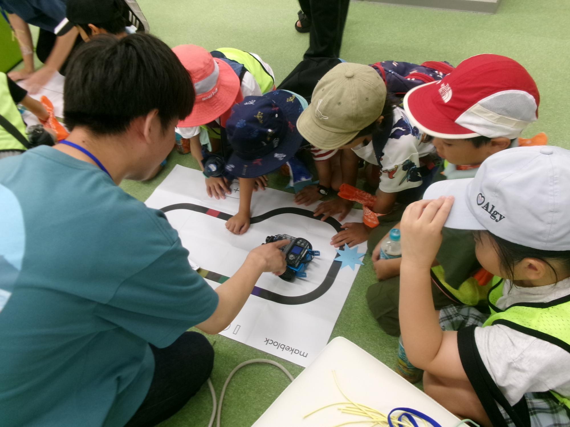 こどもたちが輪になってプログラミングロボットの動きをみている写真