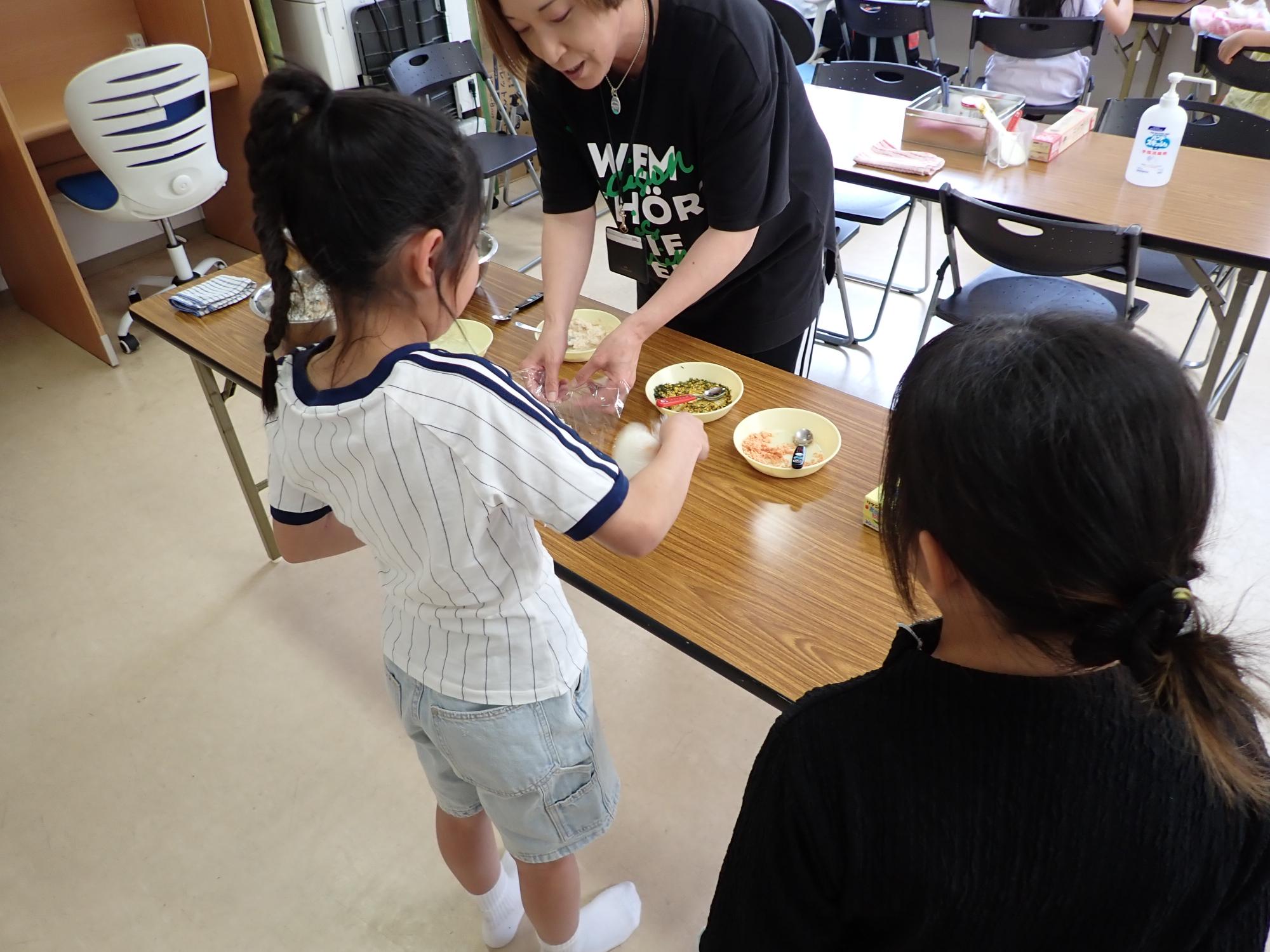 おにぎりをラップに包み、回して形を整える子どもの写真