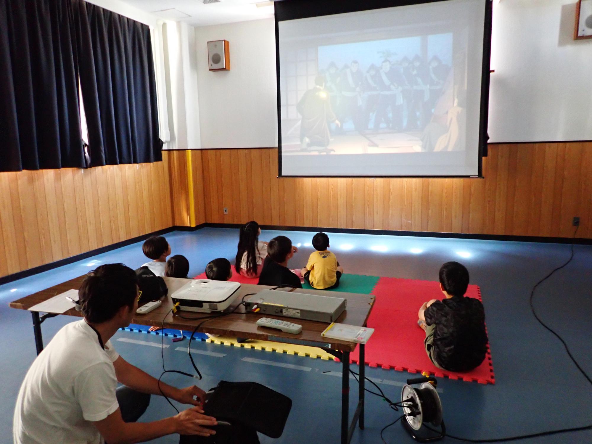 映像の機器をセッティングする職員と、映画を観る子どもたちの写真