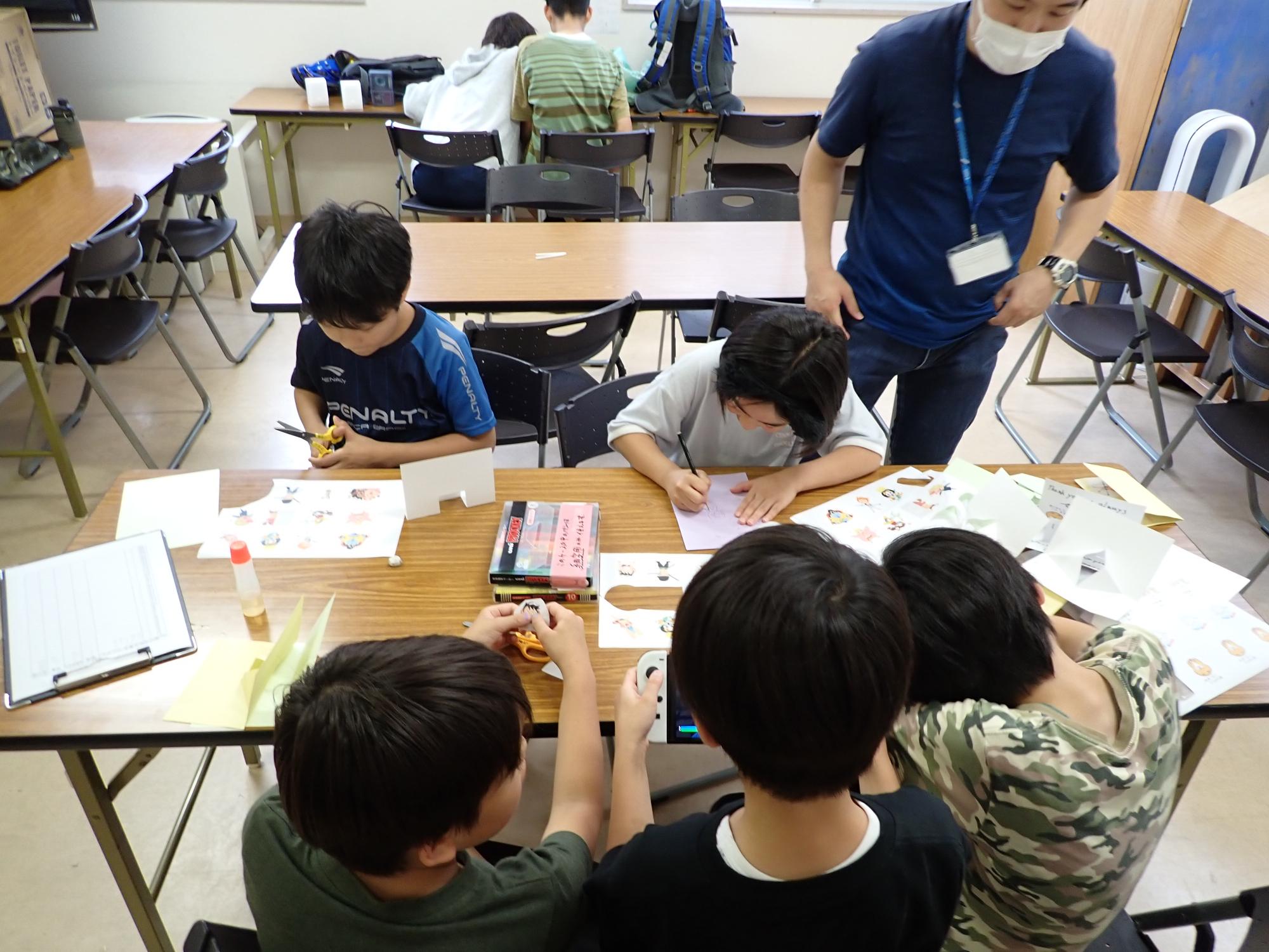 職員に作り方を聞きながら、友達と一緒にサンキューカードを作っていく子どもの写真