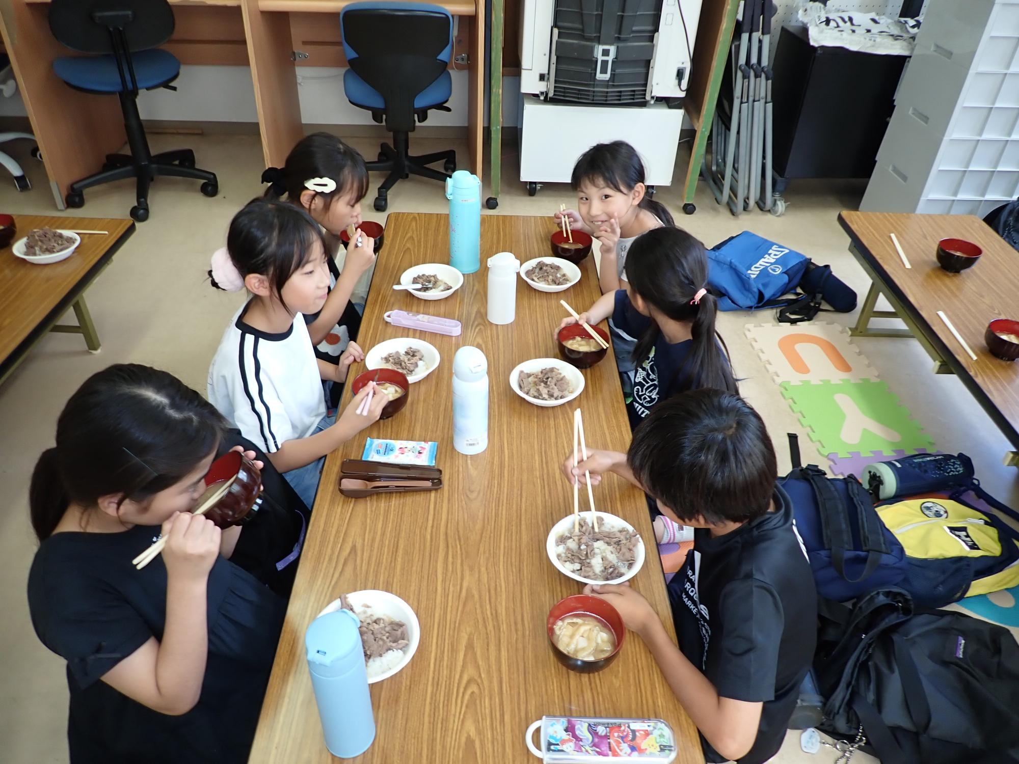 自分たちで盛りつけた牛丼とお味噌汁を食べるこどもたちの写真