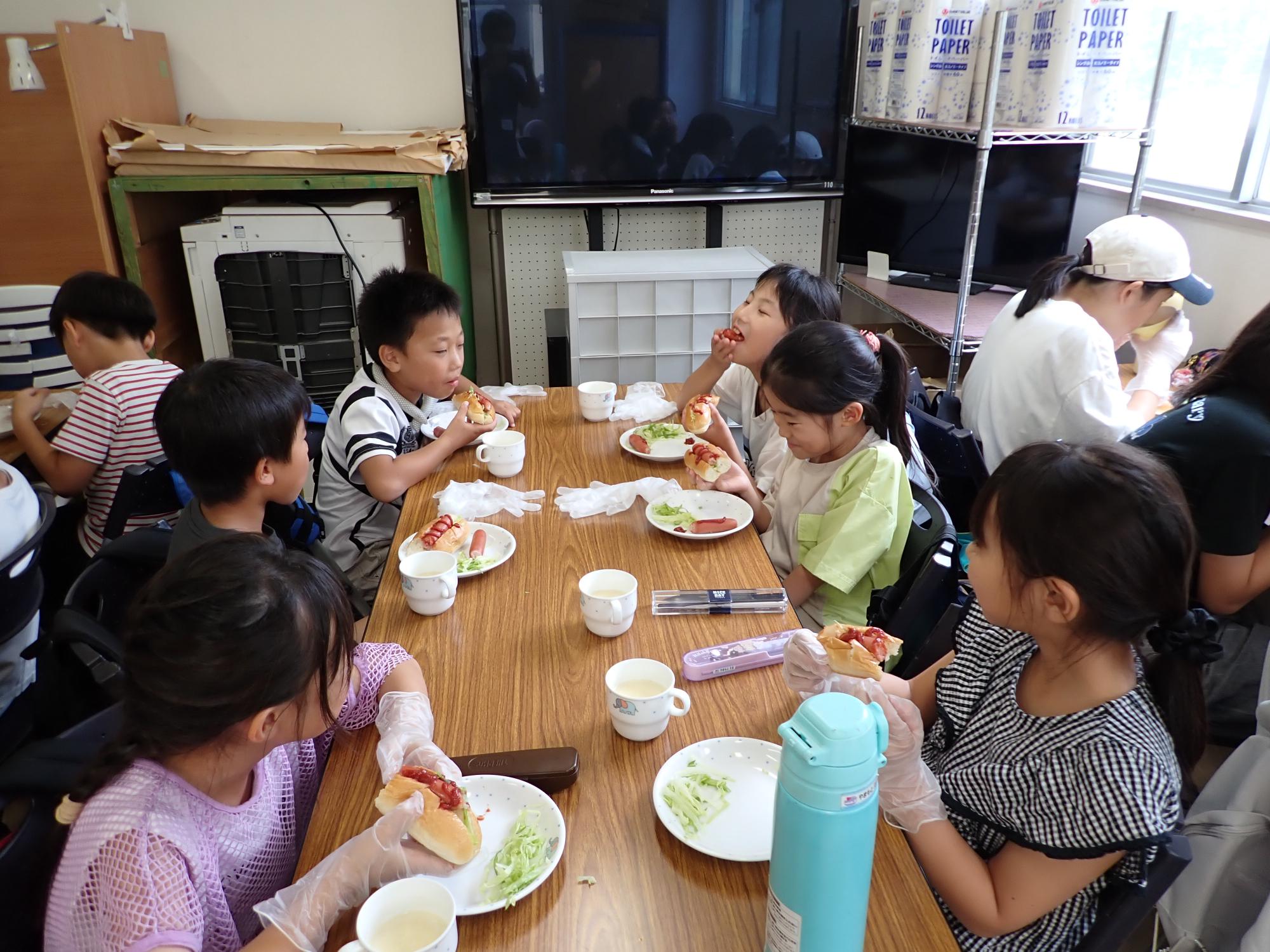 自分たちで具材をはさみ、ホットドッグを食べるこどもたちの写真