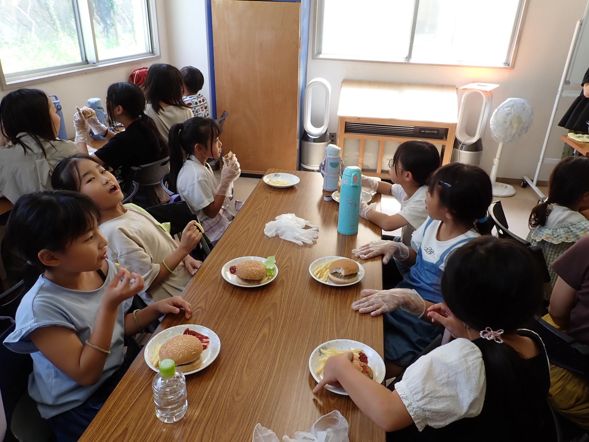自分たちで具材をはさみ、ハンバーガーを食べるこどもたちの写真