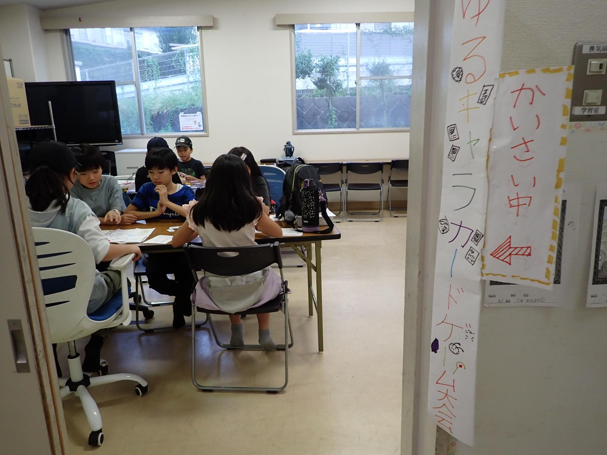 実際にカードゲームをする子どもたちと、子ども達お手製の看板の写真