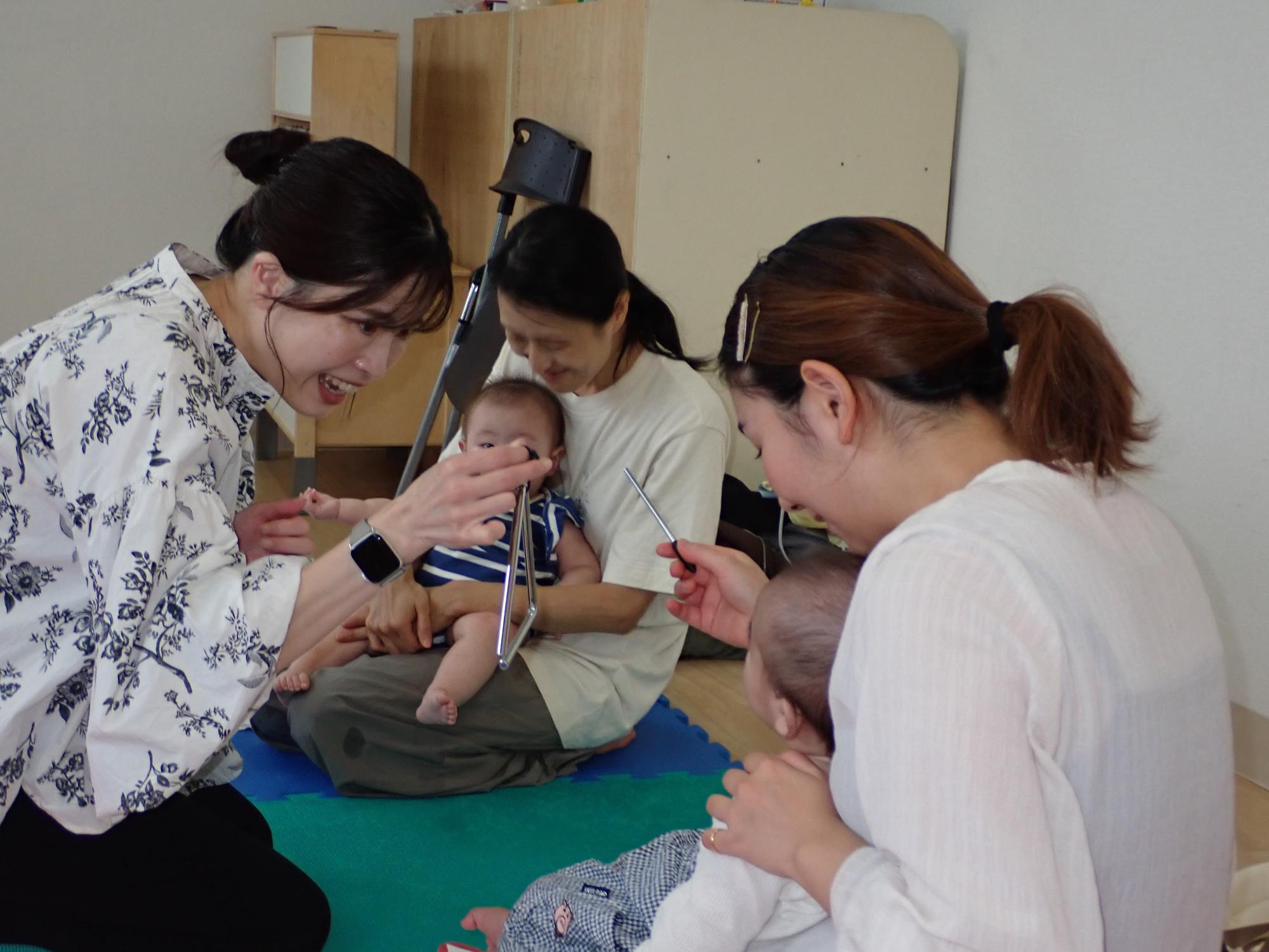 講師が持つトライアングルに興味を示す乳児さんの写真