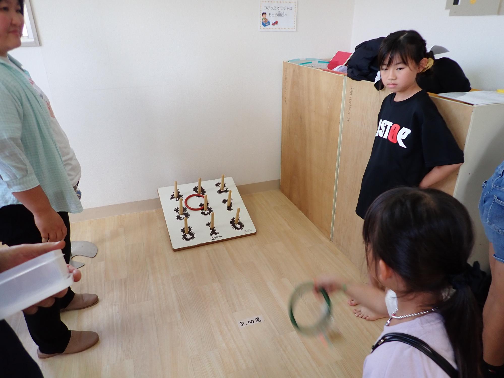 輪投げをする子どもと、それを見る子どもスタッフの写真