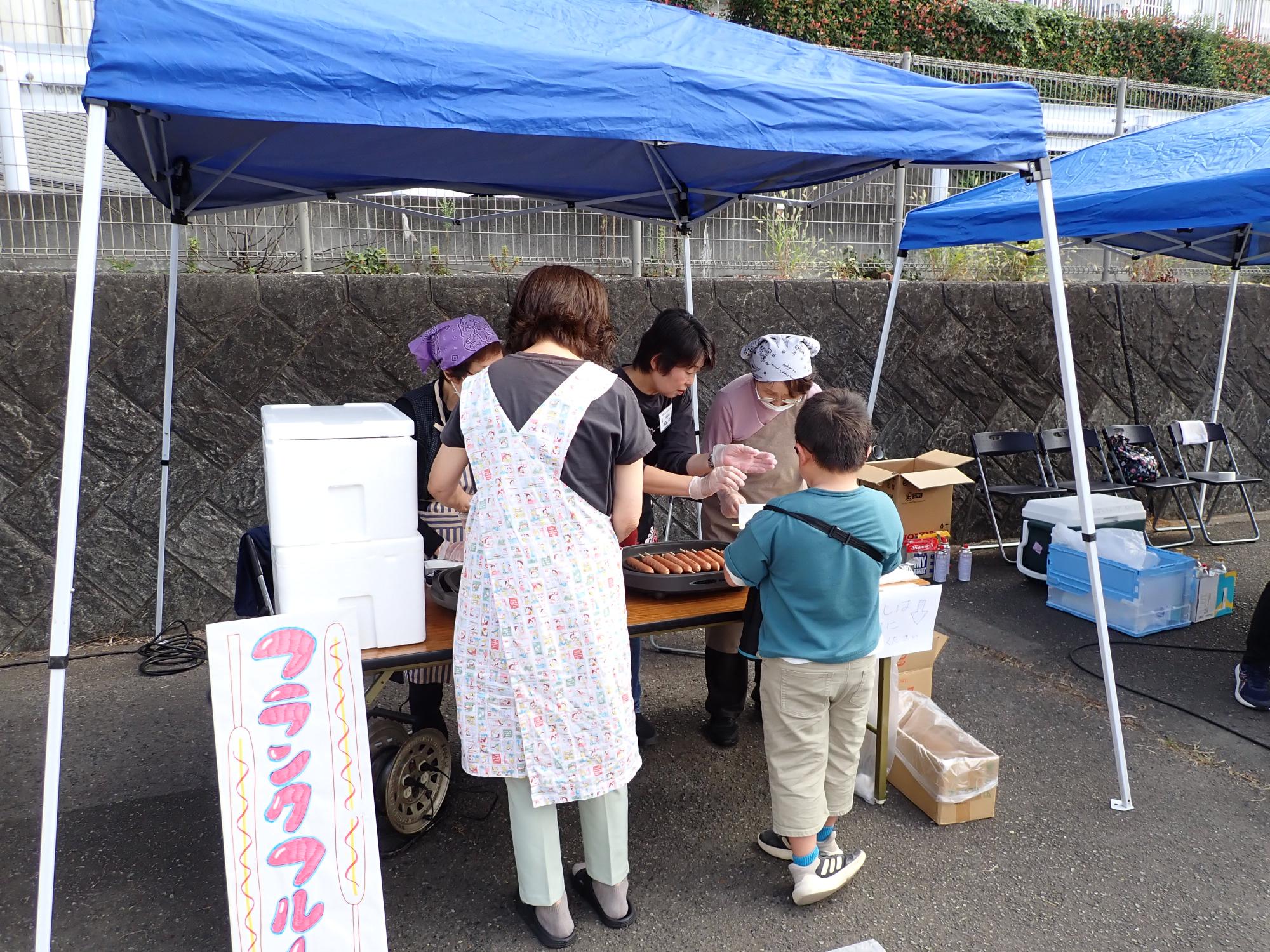 フランクフルトの販売対応をする職員と、購入する子どもの写真