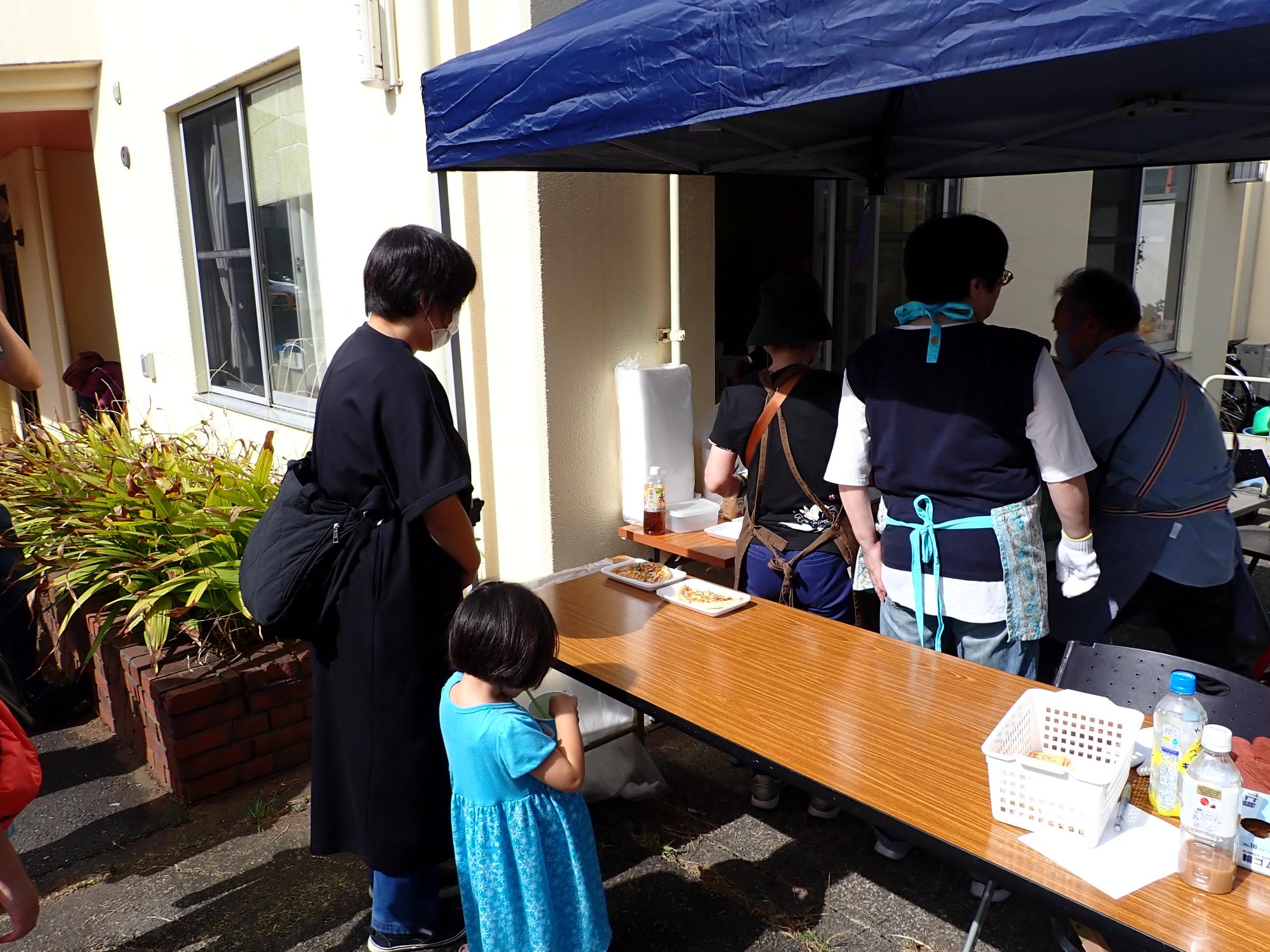 ピザを買う親子と、販売するお手伝いの方の写真