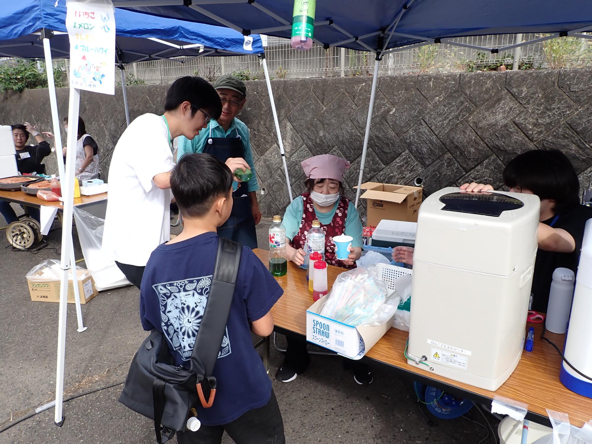 かき氷を買う子どもと、販売するお手伝いの方の写真