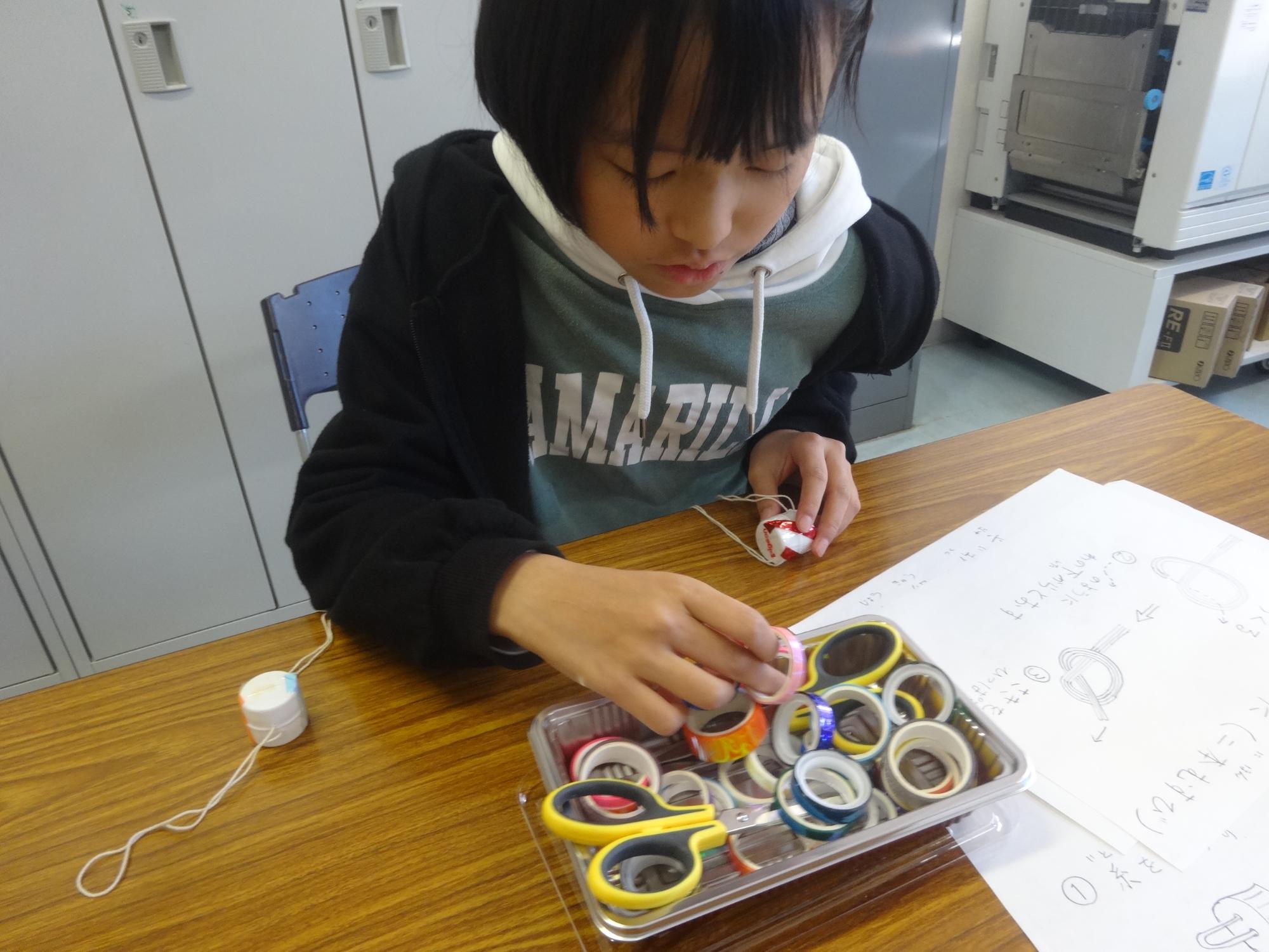 ブンブンごまの材料を選ぶ小学生の女の子の写真