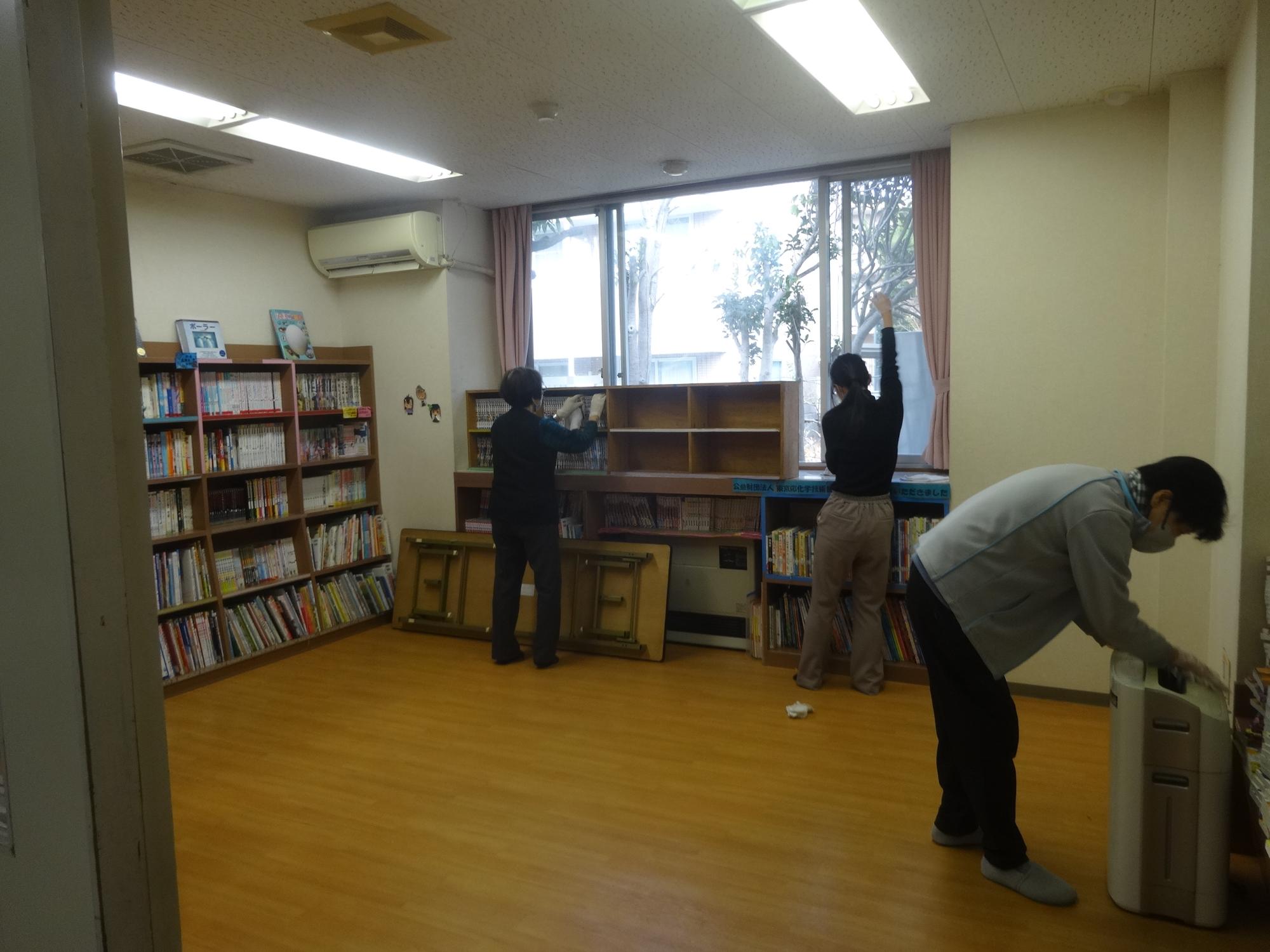 図書室の窓ふきや棚を拭いている運営協議会会員と高校生。