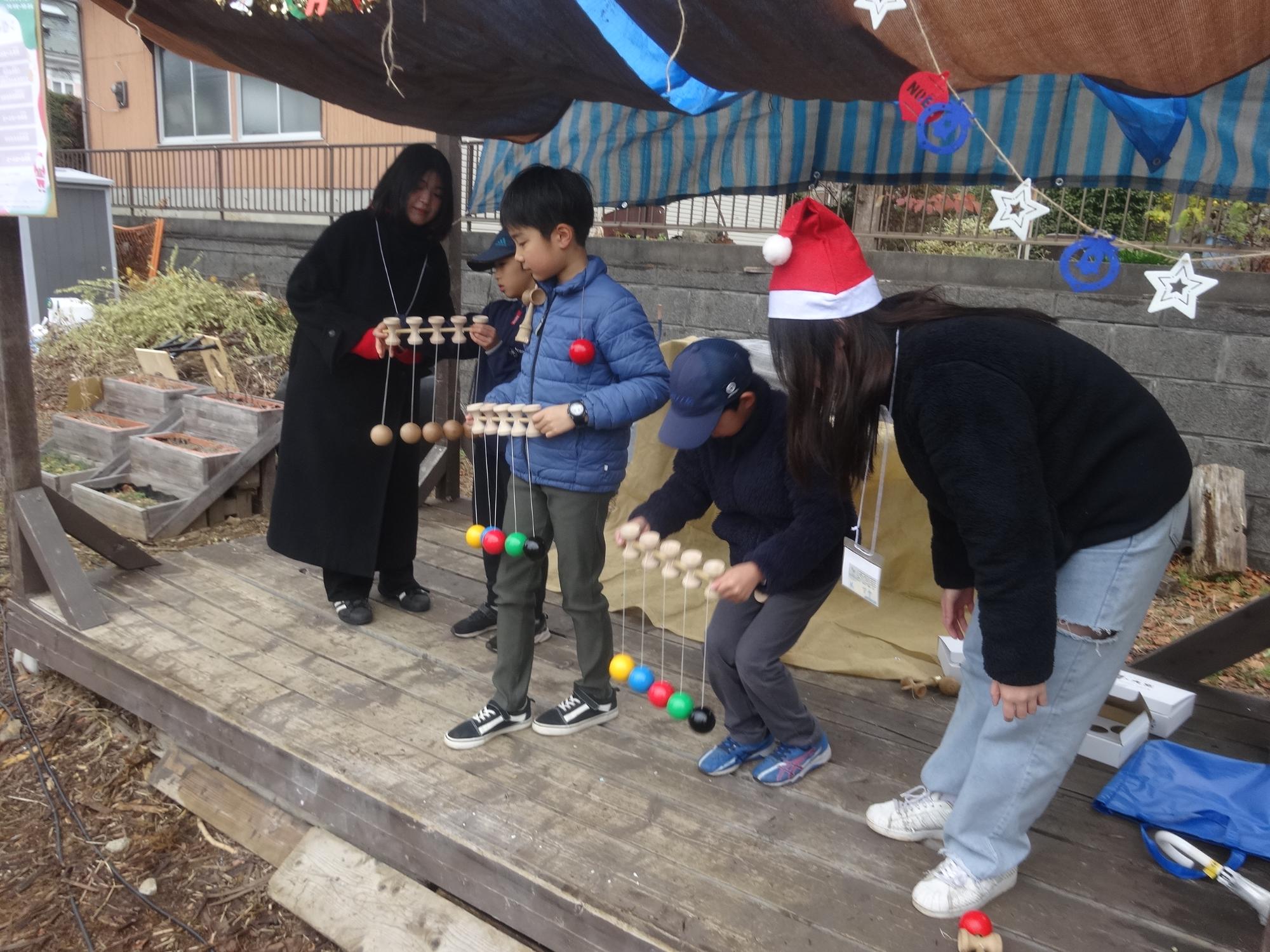 スタッフの大学生と一緒に5連けん玉をする小学生たち