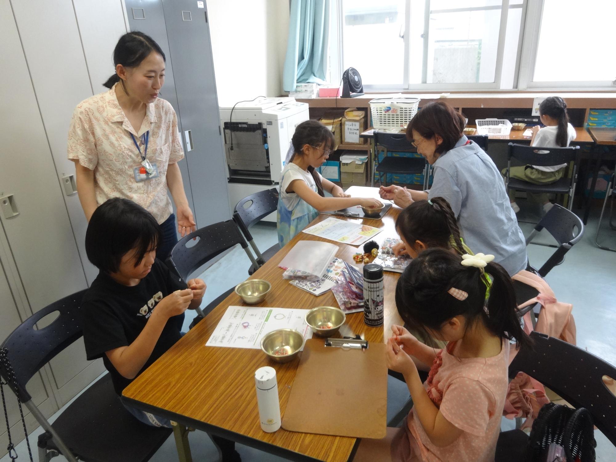 ビーズを使ってアクセサリー作りをする小学生と幼児