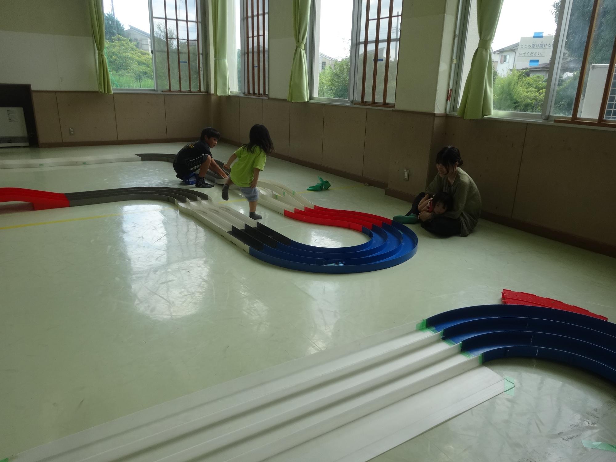 長いコースをミニ四駆が走る様子を子どもたちが眺めている