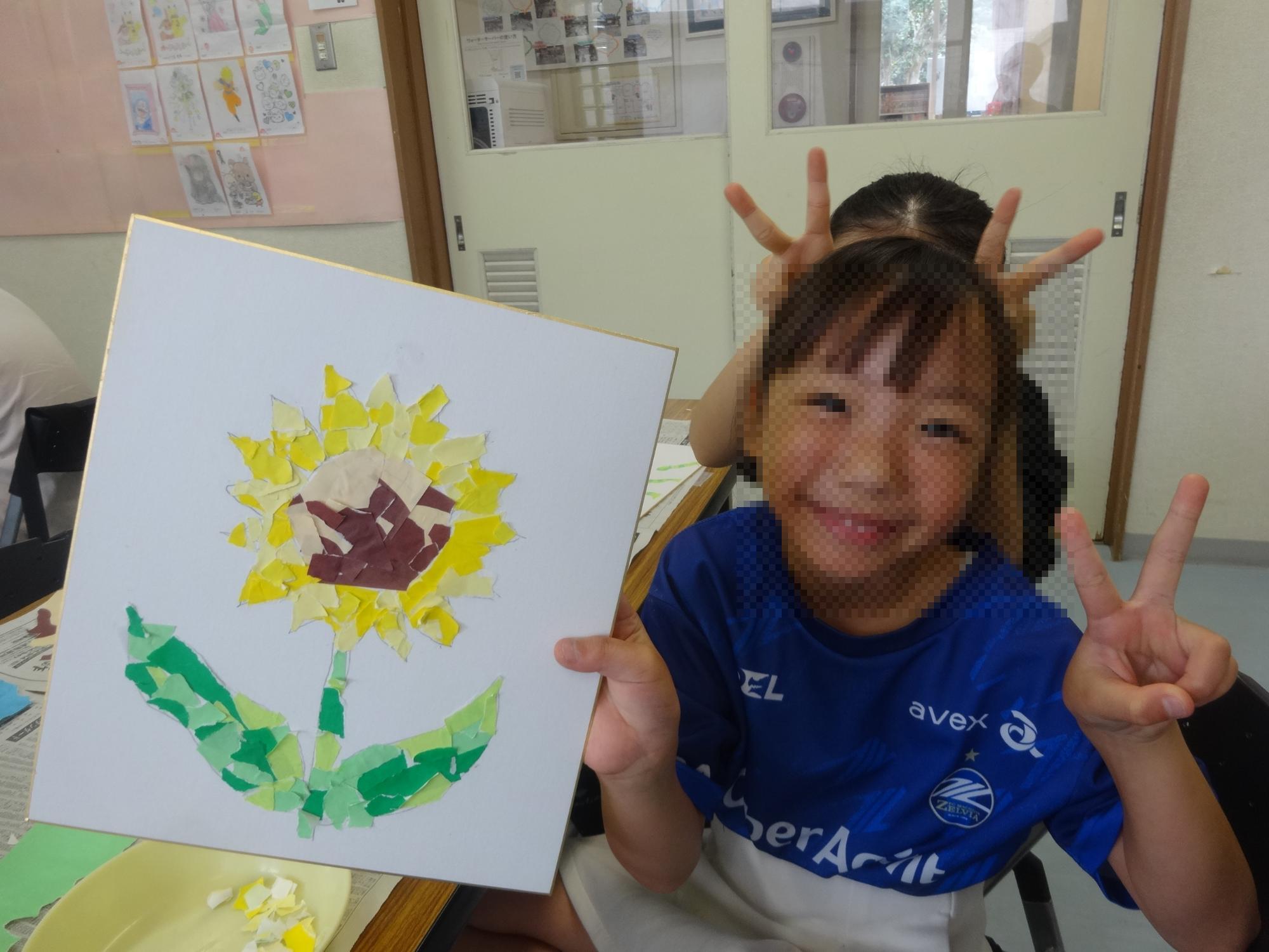 完成したひまわりのちぎり絵を持って笑顔の小学生