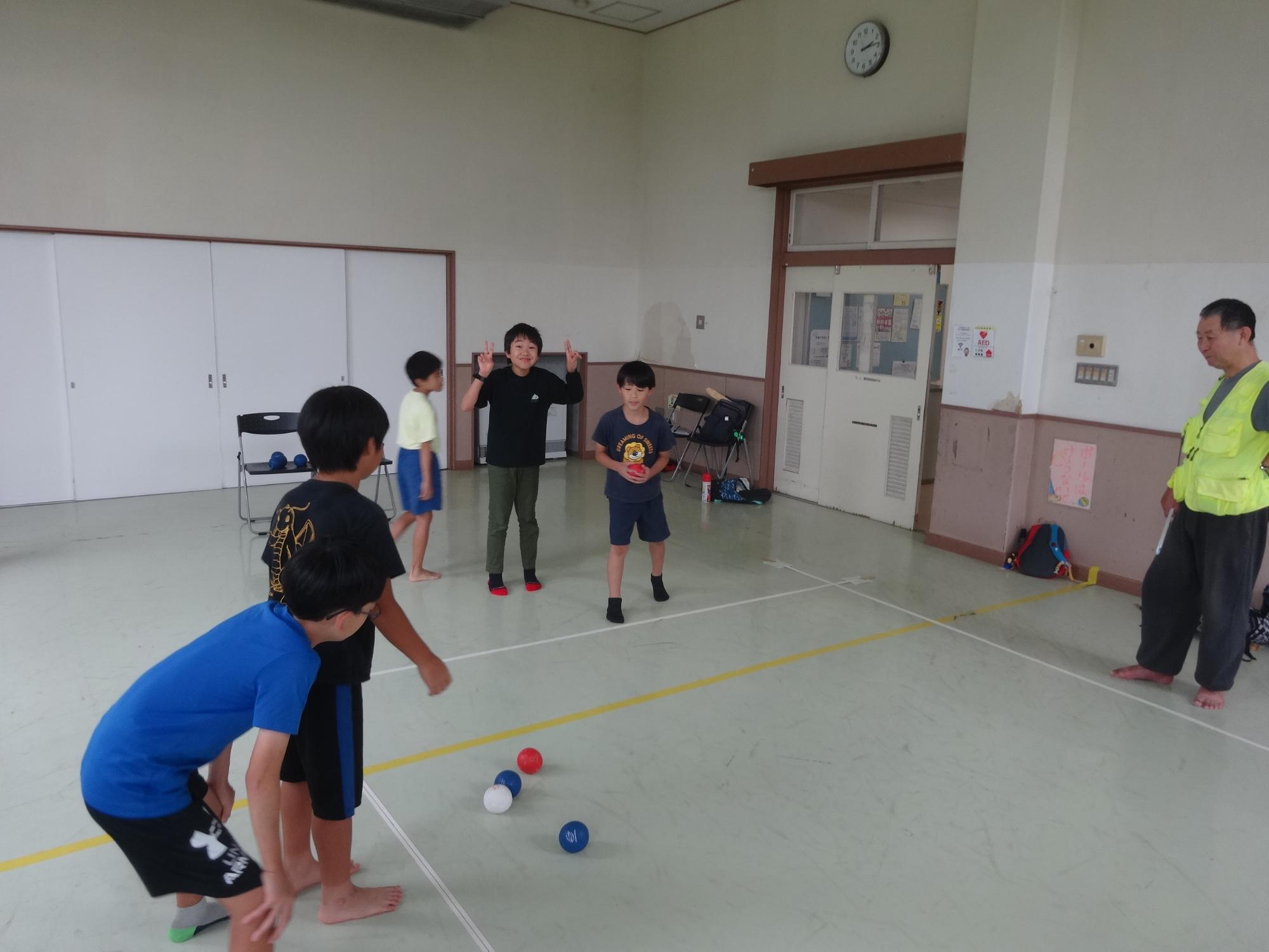 赤いボールを投げようと狙いを定める小学生と、応援をする小学生の写真