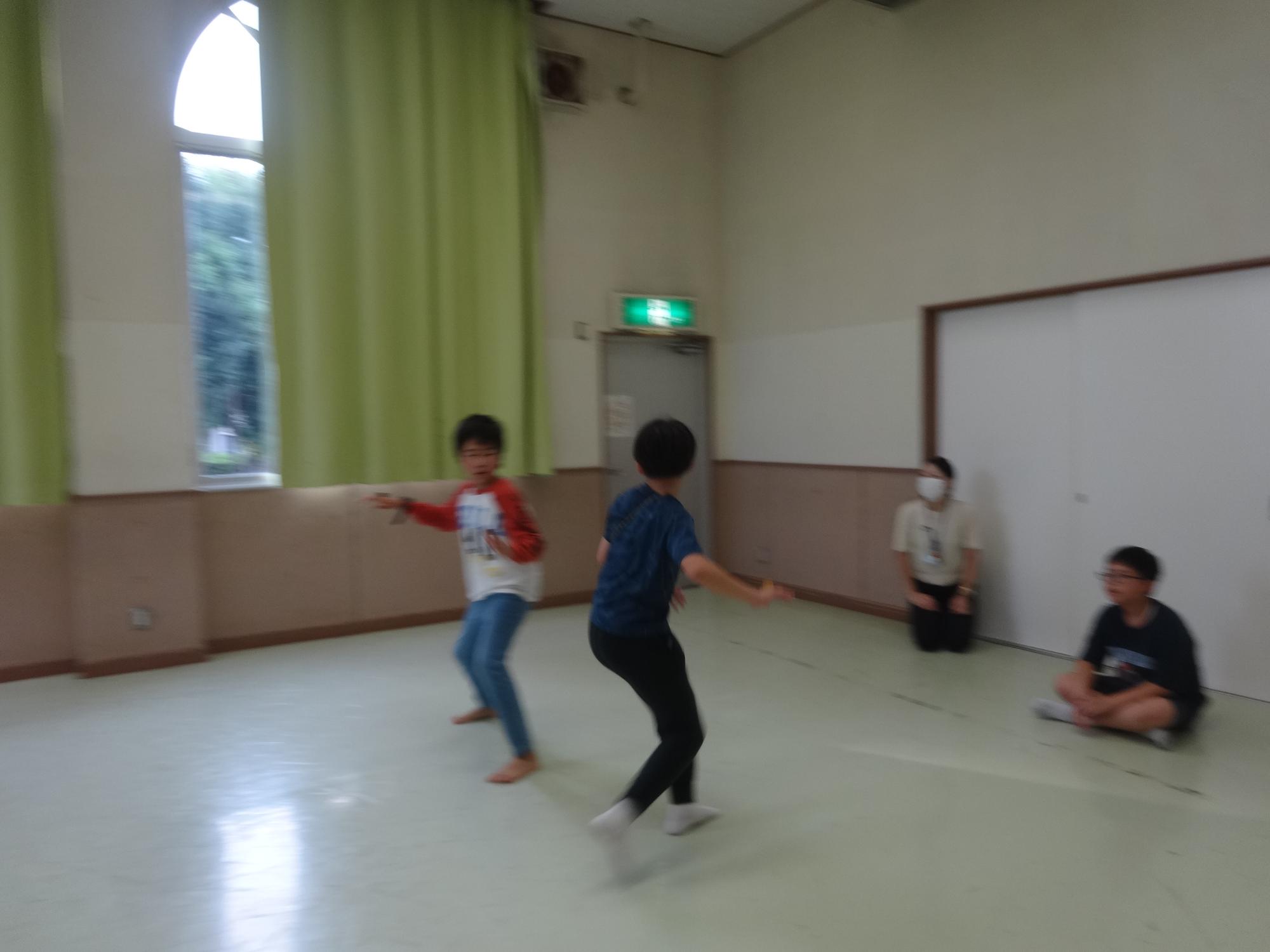 全員が片手の甲にペットボトルのキャップを乗せながら、他の人のキャップを払い落とす「キャップ落とし」で遊ぶ小学生たちの写真