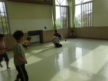 黄緑色の床の室内で、青いボールを使ってドッジボールをしている子どもたちや壁際で観戦している子どもの写真