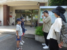 2人の男の子が2人の講師の話を建物の入り口前で聞いている写真