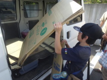 男の子が大きい段ボールを両手で車の荷台に乗せている写真