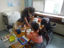 講師の男性が3人の子供たちにうちわの作り方を教えている写真