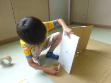 段ボールを片手で支えながらガムテープを使い建設していく男の子の写真