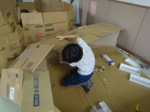 自分よりも大きい段ボールを両手を使い組み立てていく男の子の写真