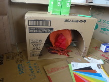 箱型にした段ボールに半径に切った入り口を付けて中に紙で作った火を置いた暖炉の作品を撮影している写真