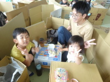 完成した段ボールハウスでお弁当を食べながら記念撮影している親子の写真
