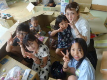 4人の女の子と母親が段ボールハウス内でピースサインで記念撮影している写真