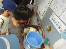 バケツに入った水をカップですくい、そのすくったカップを計量器の上に乗せる子どもの写真