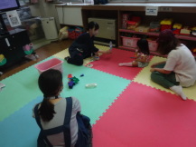 小さい子どもにおもちゃを差し出す女性と、その子どもを近くで見守るお母さんの写真
