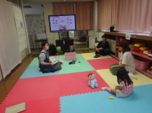 広い部屋の床に座って話をする女性たちと、そのそばに座る小さな子どもの写真