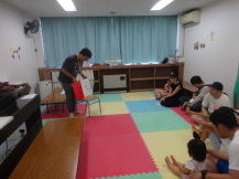 椅子の上に絵本を乗せて読み聞かせをする女性と、その女性の話を聴く参加親子の写真