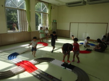 広い部屋に設置されたミニ四駆のコースと、そのコースのまわりに集まる子どもたちの写真