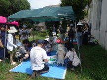 建物のそばに設置された日よけのテントの下に入る親子たちの写真