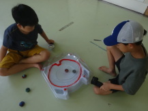 「ベイブレードスタジアム」の台の上で回っているベイブレードを対面に座った2名の子どもが見つめている写真